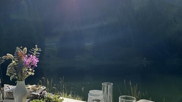 Ein schön gedeckter Tisch mit Blick auf einen See und umliegende Wälder. Die Sonne scheint hell über der Landschaft.