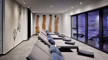 A modern relaxation room with reclining chairs and large windows. The walls are adorned with elegant wood details and floral decoration.
