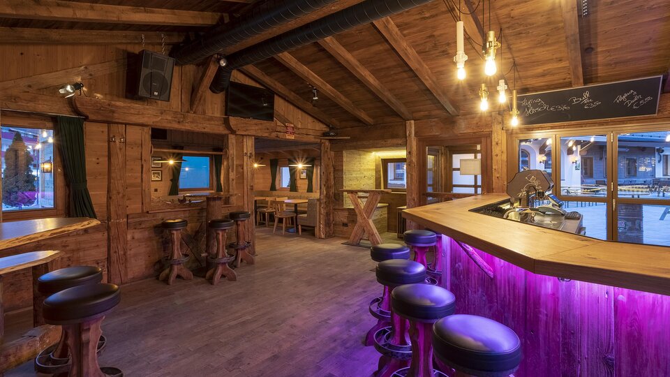 Ein gemütlicher Barbereich mit Holzinterieur und sanfter Beleuchtung. Die Bar hat eine moderne, lila beleuchtete Fläche und einige Sitzgelegenheiten.
