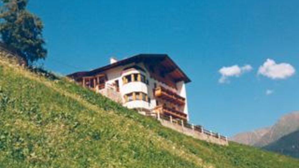 Ein schönes Haus auf einem Hügel, umgeben von grünen Wiesen. Der Himmel ist blau mit einigen Wolken.