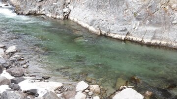 Ein klarer Fluss fließt zwischen steinigen Ufern. Das Wasser ist grünlich und die Umgebung ist von Felsen geprägt.