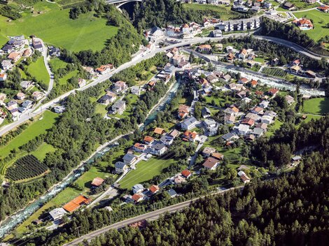 Eine malerische Ansicht eines Dorfes mit vielen Häusern und umliegender Natur. Grüne Wiesen und Wälder umgeben die ruhige Landschaft.
