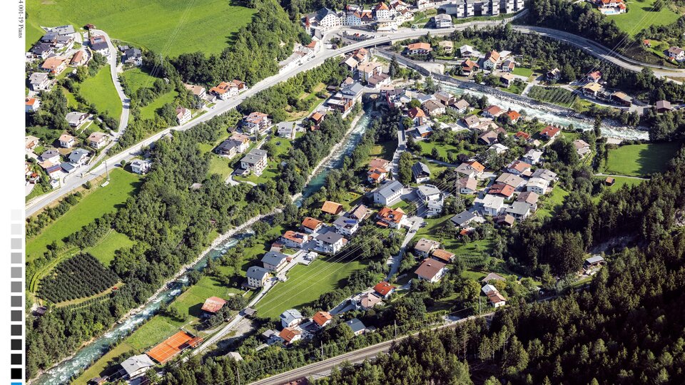 Eine malerische Ansicht eines Dorfes mit vielen Häusern und umliegender Natur. Grüne Wiesen und Wälder umgeben die ruhige Landschaft.