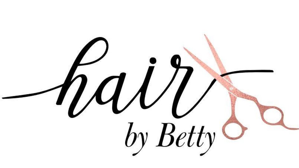 Ein schickes Logo für einen Friseursalon mit dem Namen "Hair by Betty". Es zeigt den Schriftzug in eleganter Schriftart und eine Schere.