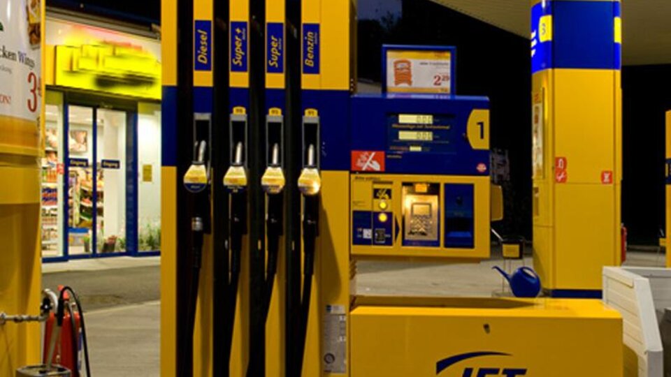 Eine Tankstelle mit mehreren Zapfsäulen und einem Kassenbereich. Es ist Abend, und die Umgebung ist gut beleuchtet.