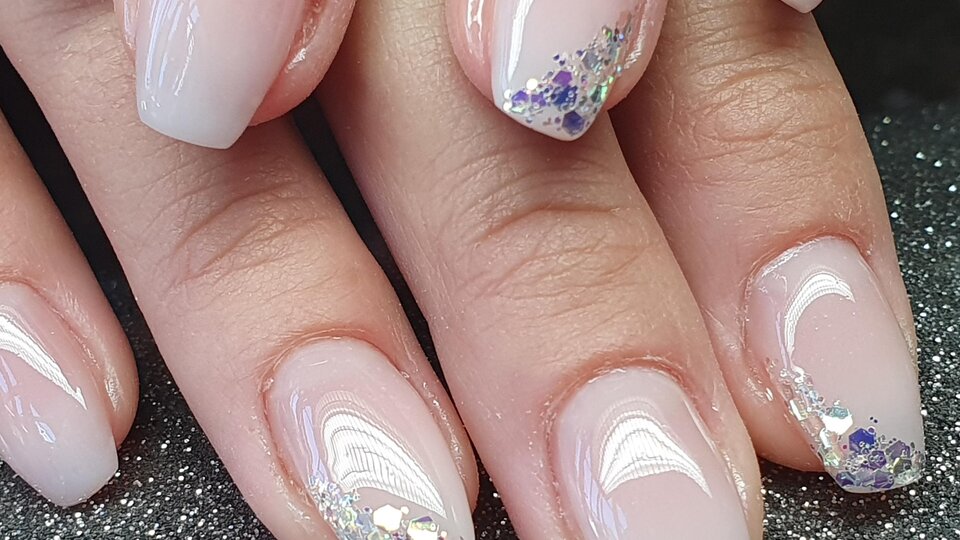 Beautiful manicure with delicate pink nails and glittering accents. The nails are neatly shaped and shine elegantly.