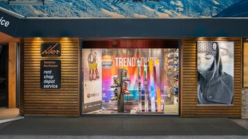 Ein Sportgeschäft mit einem Schaufenster, das Ski und Ausrüstung zeigt. Oben sind Bilder von Skifahrern und ein großes Schild mit "TRENDHOUSE".