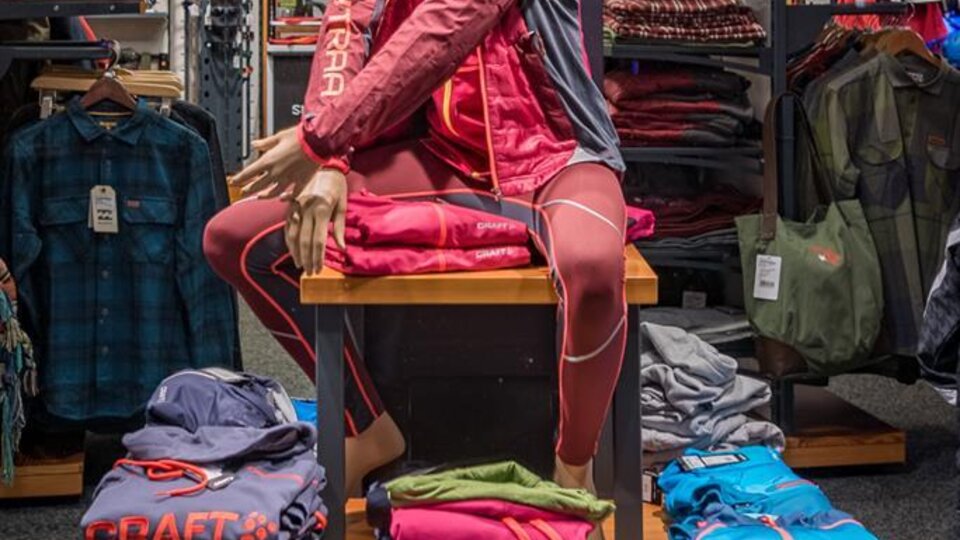 Ein Schaufenster mit einer Puppe, die Sportkleidung von Craft präsentiert. Im Hintergrund sind weitere Kleidungstücke und Accessoires angeordnet.