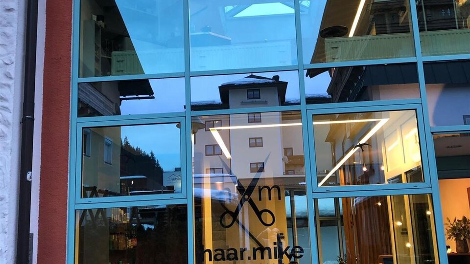 Ein modernes Friseurstudio mit großen Glasfenstern. Der Name "naar.mike" ist prominent an der Tür sichtbar.