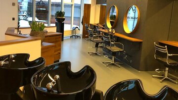 Ein moderner Friseursalon mit mehreren Waschbecken und eleganten Friseurstühlen. Große Fenster sorgen für viel natürliches Licht.